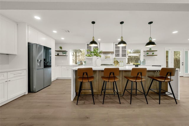 kitchen with stainless steel refrigerator with ice dispenser, light wood-type flooring, a kitchen breakfast bar, and a spacious island