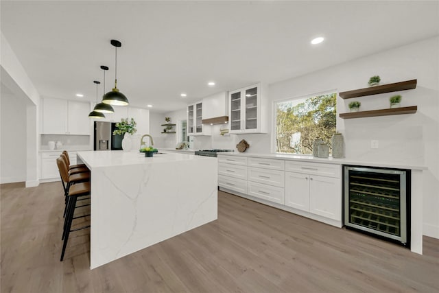 kitchen with white cabinets, an island with sink, beverage cooler, and light wood-type flooring