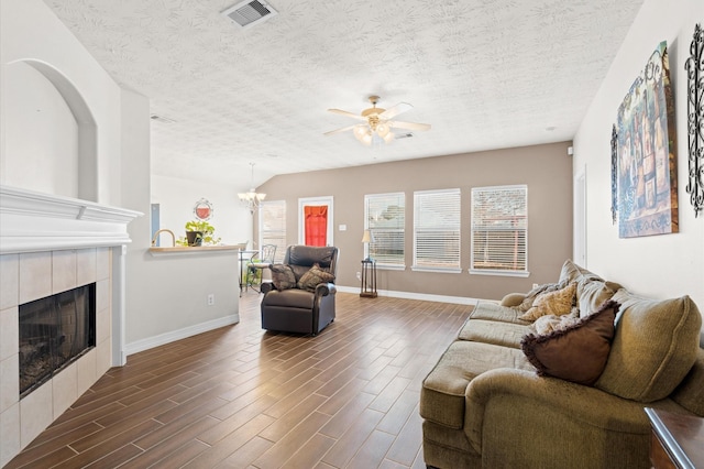 living room featuring a textured ceiling, a fireplace, and ceiling fan with notable chandelier