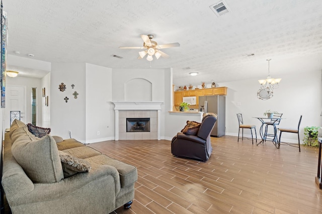 living room with ceiling fan with notable chandelier, hardwood / wood-style floors, a textured ceiling, and a fireplace