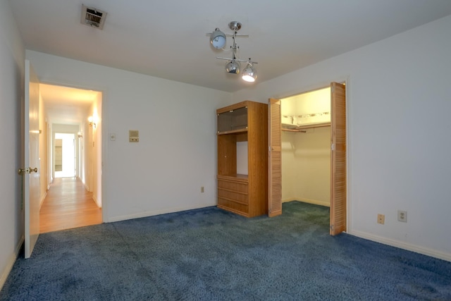 unfurnished bedroom featuring dark carpet, a walk in closet, and a closet