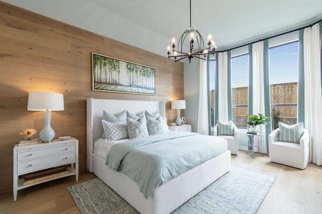 bedroom with wood walls, light hardwood / wood-style floors, and an inviting chandelier