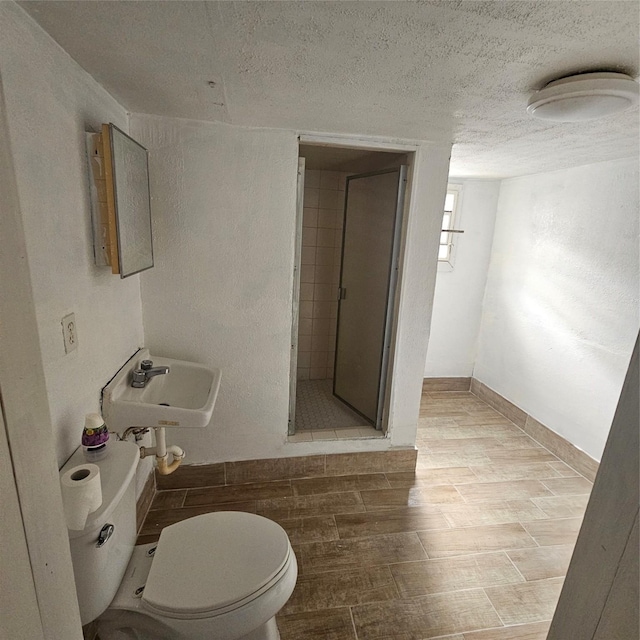 bathroom with a textured ceiling, tiled shower, toilet, and sink