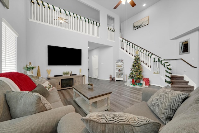 living area with a ceiling fan, a high ceiling, stairway, and wood finished floors