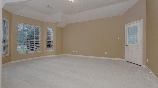 empty room with lofted ceiling, light colored carpet, baseboards, and a textured ceiling