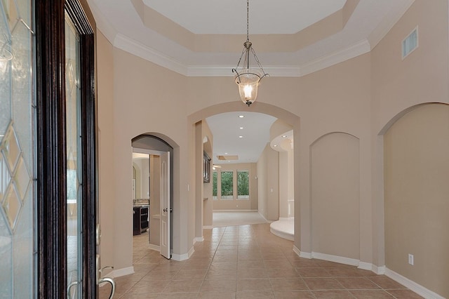 corridor featuring visible vents, baseboards, a tray ceiling, a towering ceiling, and light tile patterned flooring