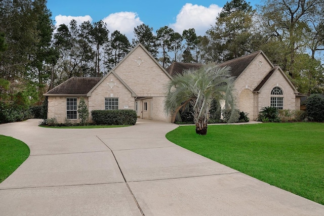 french country home with a front lawn, concrete driveway, and brick siding