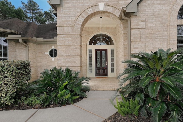 view of exterior entry featuring brick siding and roof with shingles