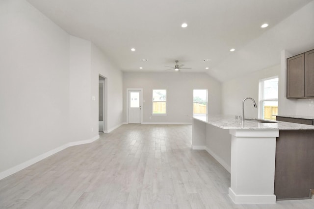 kitchen with lofted ceiling, sink, ceiling fan, light stone countertops, and light hardwood / wood-style floors