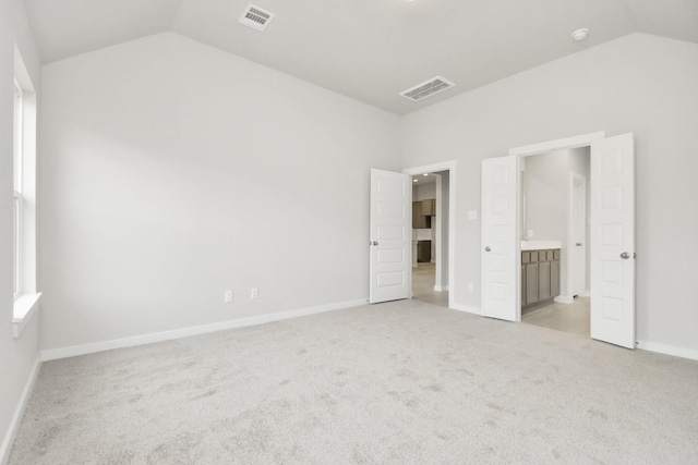 unfurnished bedroom with lofted ceiling, light carpet, and connected bathroom