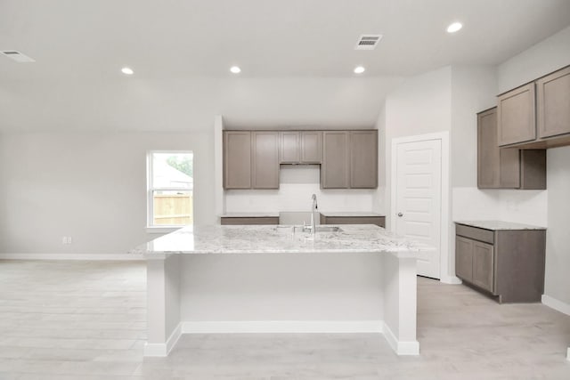 kitchen with light stone countertops, a center island with sink, vaulted ceiling, and sink