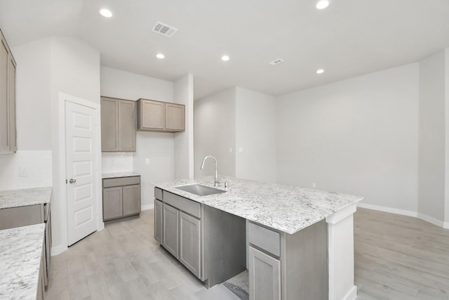 kitchen featuring sink, tasteful backsplash, light hardwood / wood-style floors, gray cabinets, and a kitchen island with sink