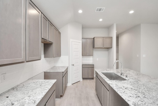 kitchen featuring decorative backsplash, light stone counters, light hardwood / wood-style flooring, and sink