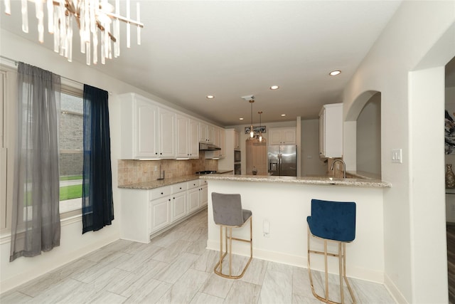 kitchen with white cabinetry, hanging light fixtures, light stone counters, stainless steel refrigerator with ice dispenser, and decorative backsplash