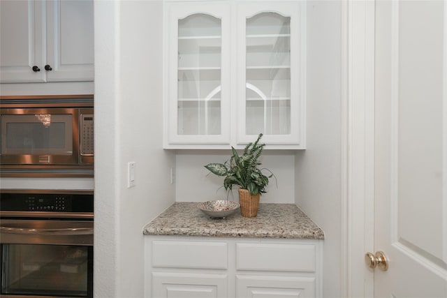 bar featuring white cabinets, black oven, stainless steel microwave, and light stone countertops