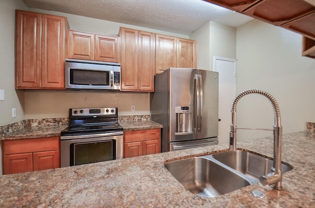 kitchen featuring light stone countertops, sink, stainless steel appliances, and a textured ceiling