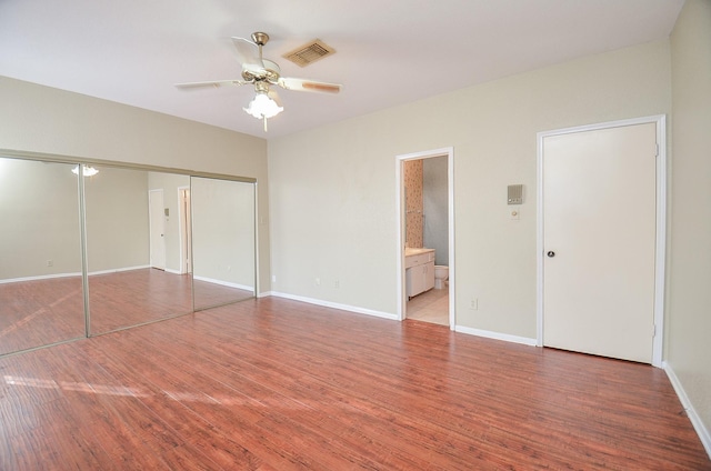 unfurnished bedroom featuring hardwood / wood-style flooring, ceiling fan, ensuite bath, and a closet