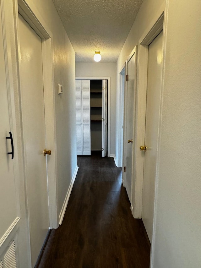 hallway with a textured ceiling and dark hardwood / wood-style floors