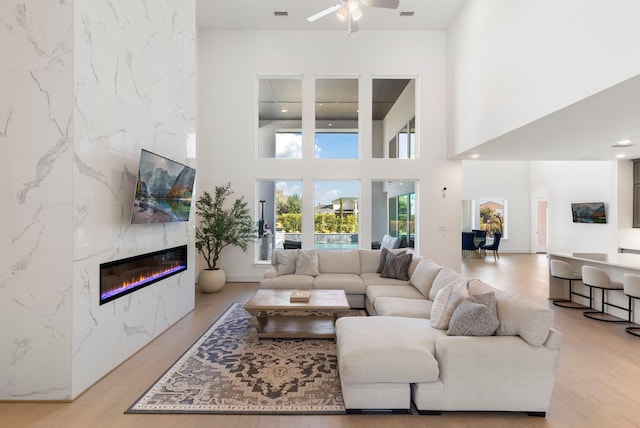 living room featuring ceiling fan, a high ceiling, a high end fireplace, and light hardwood / wood-style flooring