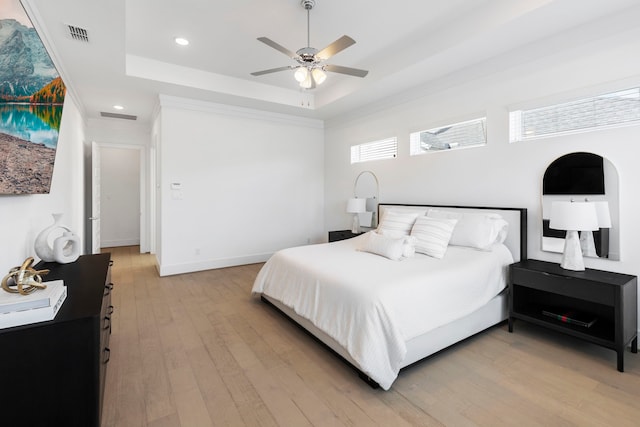 bedroom with ceiling fan, a raised ceiling, and light hardwood / wood-style flooring