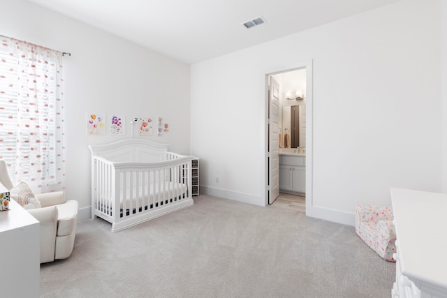 bedroom with ensuite bathroom, light colored carpet, and a crib