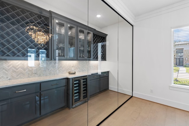 bar featuring backsplash, light wood-type flooring, ornamental molding, beverage cooler, and a chandelier