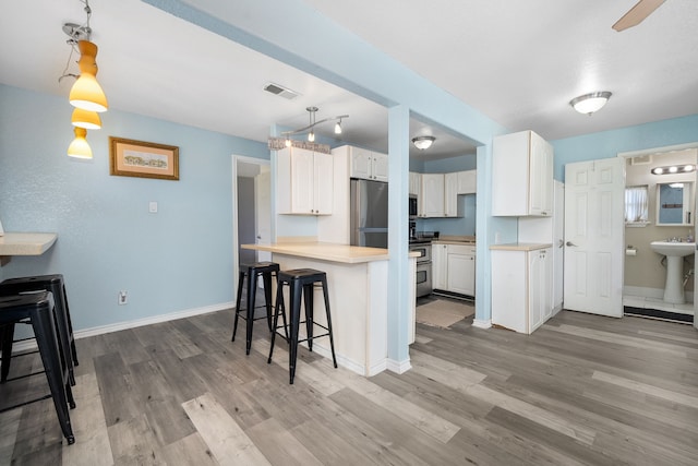 kitchen with white cabinets, appliances with stainless steel finishes, a kitchen bar, and light wood-type flooring