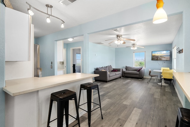 kitchen with kitchen peninsula, ceiling fan, wood-type flooring, white cabinetry, and a breakfast bar area