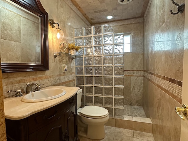 bathroom with vanity, toilet, a tile shower, and tile walls