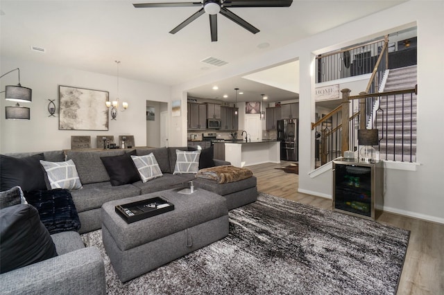 living room with wine cooler, sink, wood-type flooring, and ceiling fan with notable chandelier