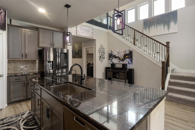 kitchen featuring pendant lighting, sink, dark stone countertops, light wood-type flooring, and stainless steel fridge with ice dispenser