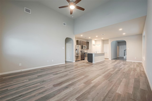 unfurnished living room with ceiling fan, a high ceiling, and light wood-type flooring