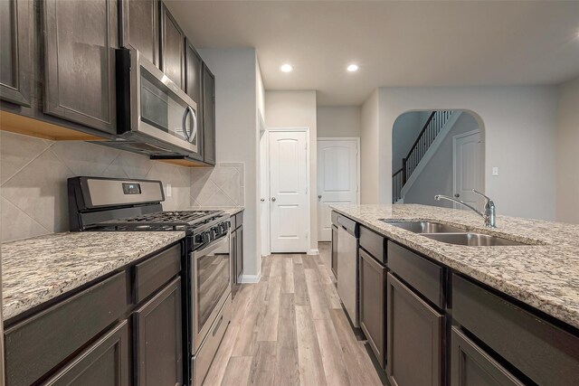 kitchen with sink, light hardwood / wood-style flooring, light stone countertops, appliances with stainless steel finishes, and dark brown cabinetry