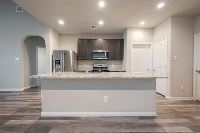 kitchen featuring dark brown cabinets, light wood-type flooring, an island with sink, and appliances with stainless steel finishes