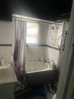 bathroom with vanity, shower / bathtub combination with curtain, and tile walls