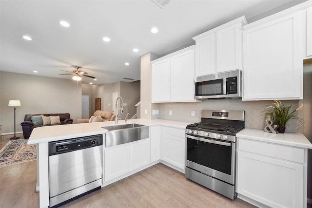 kitchen with kitchen peninsula, sink, light hardwood / wood-style flooring, appliances with stainless steel finishes, and white cabinetry