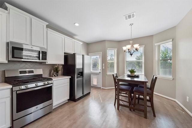 kitchen featuring white cabinets, appliances with stainless steel finishes, a chandelier, and light hardwood / wood-style floors