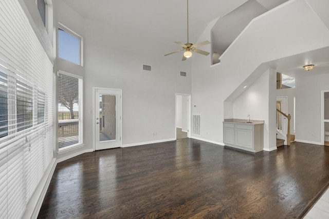 unfurnished living room with ceiling fan, dark wood-type flooring, and a high ceiling