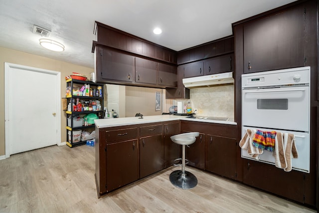 kitchen with kitchen peninsula, light hardwood / wood-style flooring, double oven, cooktop, and dark brown cabinetry