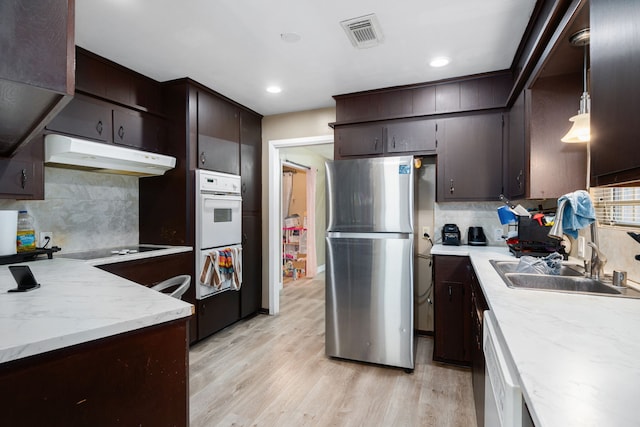 kitchen featuring tasteful backsplash, white appliances, sink, decorative light fixtures, and light hardwood / wood-style floors