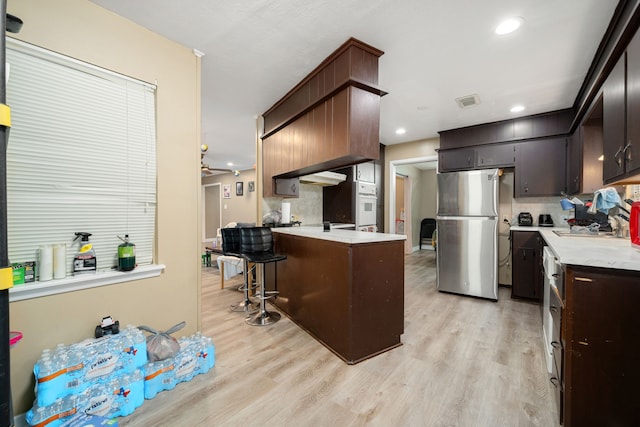 kitchen featuring a kitchen breakfast bar, sink, decorative backsplash, light wood-type flooring, and stainless steel refrigerator