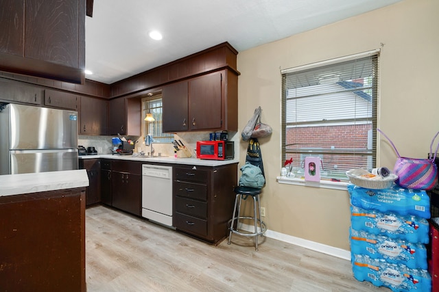 kitchen with light wood-type flooring, white dishwasher, stainless steel refrigerator, and plenty of natural light