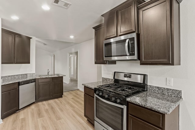 kitchen with light wood-type flooring, light stone counters, dark brown cabinets, stainless steel appliances, and sink