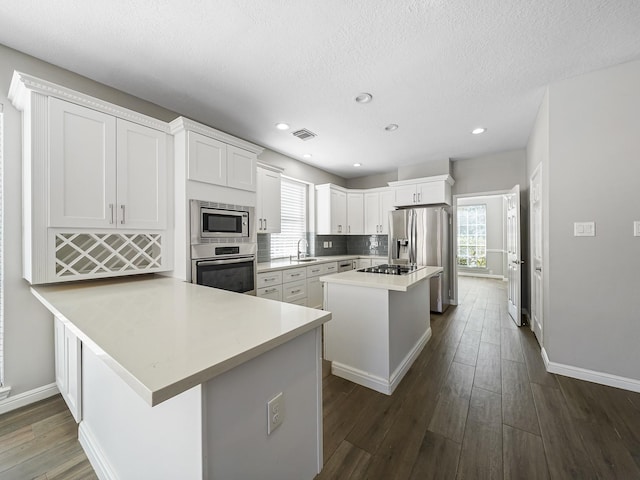 kitchen with a center island, dark wood-type flooring, kitchen peninsula, appliances with stainless steel finishes, and white cabinetry