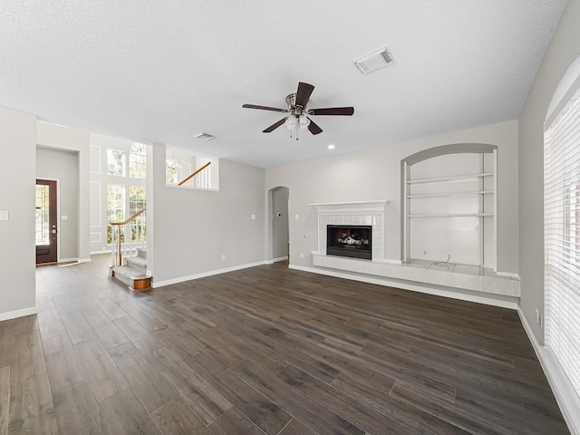 unfurnished living room featuring a textured ceiling, built in shelves, ceiling fan, and dark hardwood / wood-style floors