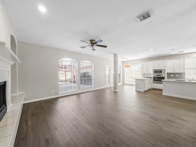 unfurnished living room with hardwood / wood-style flooring, ceiling fan, a textured ceiling, and a tile fireplace