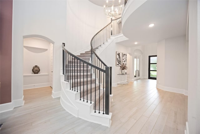 staircase featuring hardwood / wood-style floors, a towering ceiling, and an inviting chandelier