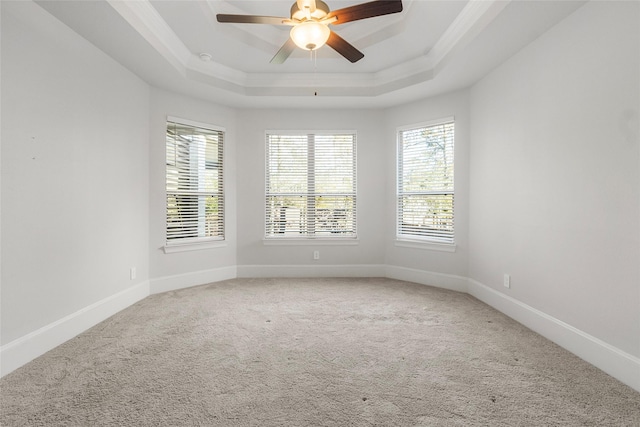 carpeted empty room featuring crown molding, baseboards, a raised ceiling, and a ceiling fan