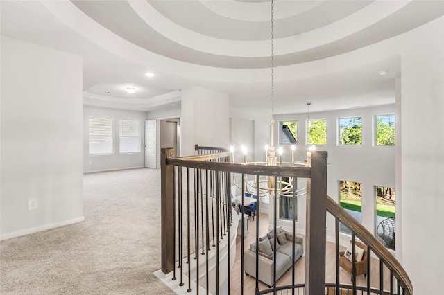 hall with plenty of natural light, baseboards, carpet, a tray ceiling, and an upstairs landing