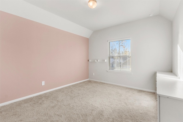 carpeted spare room featuring vaulted ceiling and baseboards